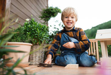 Portrait of happy small boy outdoors on table constructing birdhouse, diy project. - HPIF14802