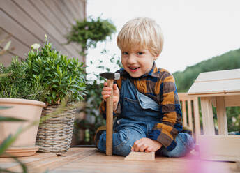 Portrait of happy small boy outdoors on table constructing birdhouse, diy project. - HPIF14803