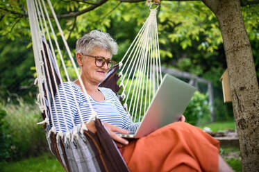 Seitenansicht Porträt der aktiven älteren Frau mit Laptop arbeiten im Freien im Garten, Home-Office-Konzept. - HPIF14805