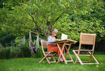 Active senior woman with laptop working at the table outdoors in garden, home office concept. - HPIF14813