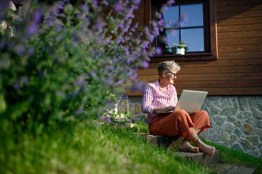 Glückliche ältere Frau mit Laptop arbeitet im Freien im Garten, Home-Office-Konzept. - HPIF14820