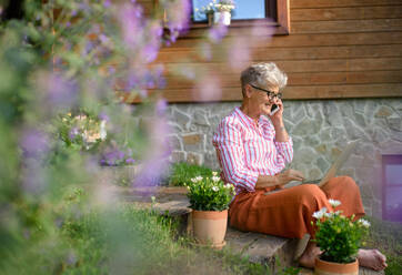 Glückliche ältere Frau mit Laptop, Smartphone arbeiten im Freien im Garten, Home-Office-Konzept. - HPIF14821