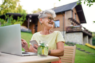 Glückliche ältere Frau mit Laptop, Smartphone arbeiten im Freien im Garten, Home-Office-Konzept. - HPIF14830