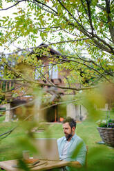 Seitenansicht von reifen Mann mit Laptop arbeiten im Freien im Garten, Home-Office-Konzept. - HPIF14833