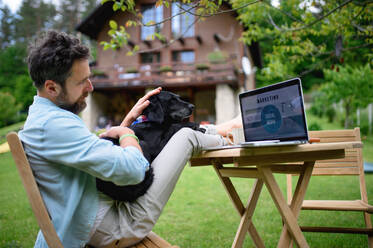 Glücklicher reifer Mann mit Laptop und Hund bei der Arbeit im Freien im Garten, Home-Office-Konzept. - HPIF14836