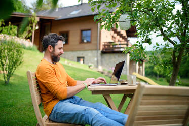 Side view of mature man with laptop working outdoors in garden, home office concept. - HPIF14842