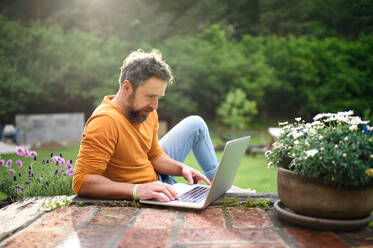 Glücklicher reifer Mann mit Laptop arbeitet draußen im Garten, Home-Office-Konzept. - HPIF14844