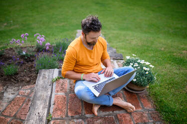 Draufsicht auf einen reifen Mann mit Laptop, der draußen im Garten arbeitet, Home-Office-Konzept. - HPIF14845