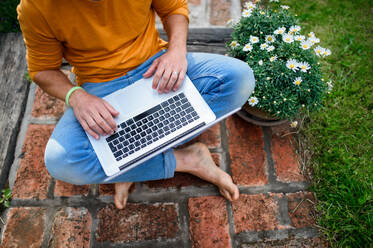 Top view of unrecognizable man with laptop working outdoors in garden, home office concept. - HPIF14846