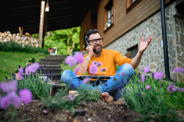 Porträt eines reifen Mannes mit Laptop und Smartphone bei der Arbeit im Garten, Home-Office-Konzept. - HPIF14850