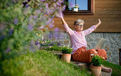 Eine glückliche ältere Frau mit Laptop arbeitet im Freien im Garten, Home-Office-Konzept. - HPIF14872