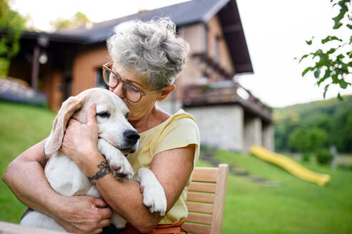 A close-up portrait of senior woman sitting outdoors in garden, pet dog friendship concept. - HPIF14883