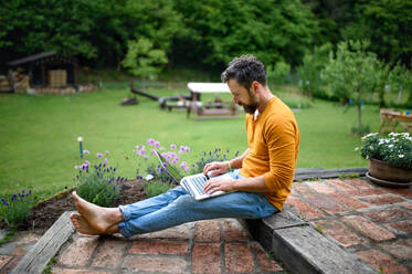 Porträt eines reifen Mannes mit Laptop, der im Freien im Garten arbeitet, grünes Home-Office-Konzept. - HPIF14888