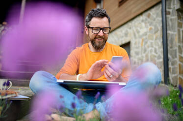 Porträt eines reifen Mannes mit Smartphone bei der Arbeit im Freien im Garten, grünes Home-Office-Konzept. - HPIF14892