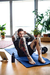 Frontansicht Porträt eines jungen Mannes mit Tablet tun Workout-Übung drinnen zu Hause. - HPIF14899