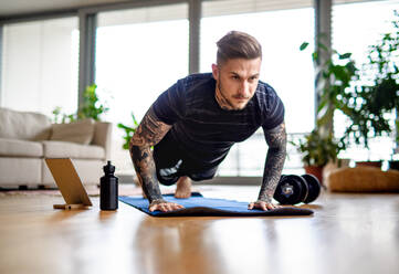 Frontansicht Porträt eines jungen Mannes mit Tablet tun Workout-Übung drinnen zu Hause. - HPIF14901