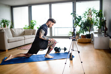 Young man trainer doing online workout exercise indoors at home, using camera. - HPIF14902