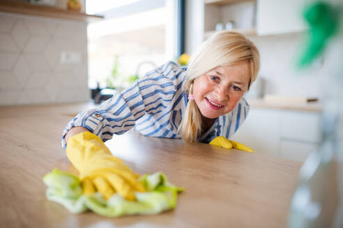 Porträt einer glücklichen älteren Frau, die zu Hause die Arbeitsplatte der Küchenzeile reinigt. - HPIF14931