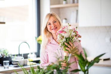 Porträt einer glücklichen älteren Frau, die zu Hause Blumen in einer Vase arrangiert. - HPIF14942