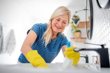 Happy senior woman with gloves cleaning bathroom indoors at home. - HPIF14948