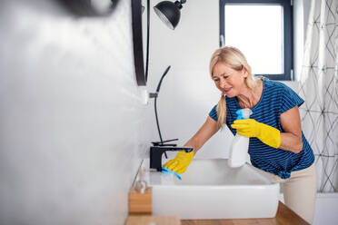 Happy senior woman with gloves cleaning bathroom indoors at home. - HPIF14950