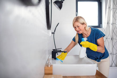 Glückliche ältere Frau mit Handschuhen beim Putzen des Badezimmers zu Hause. - HPIF14950