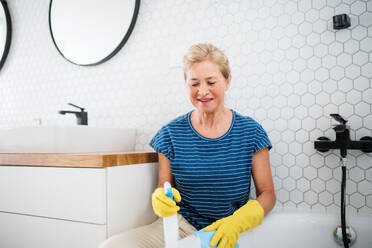 Happy senior woman with gloves cleaning bathroom indoors at home. - HPIF14951