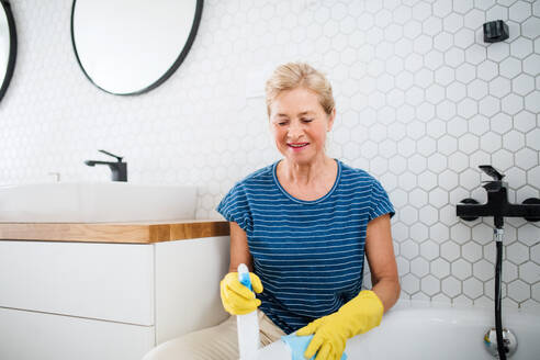 Glückliche ältere Frau mit Handschuhen beim Putzen des Badezimmers zu Hause. - HPIF14951