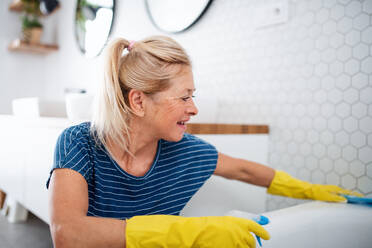 Glückliche ältere Frau mit Handschuhen beim Putzen des Badezimmers zu Hause. - HPIF14952