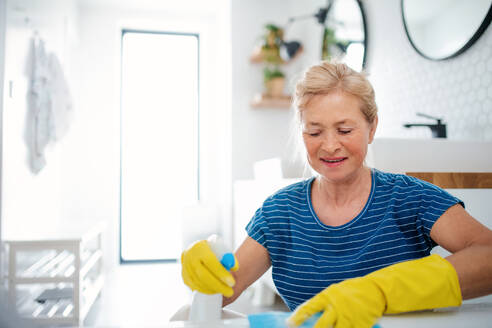 Glückliche ältere Frau mit Handschuhen beim Putzen des Badezimmers zu Hause. - HPIF14953