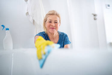 Happy senior woman with gloves cleaning bathroom indoors at home. - HPIF14955