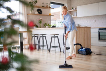 Glückliche ältere Frau mit Staubsauger zu Hause in der Weihnachtszeit beim Staubsaugen. - HPIF14962