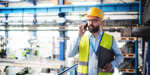 Ein Techniker oder Ingenieur mit Schutzmaske und Telefon bei der Arbeit in einem Industriebetrieb. - HPIF14995