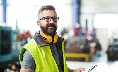 Technician or engineer with protective headphones standing in industrial factory. Copy space. - HPIF15030