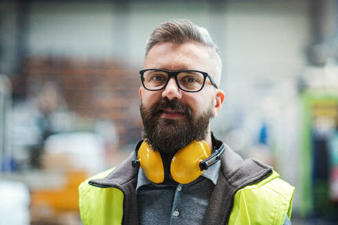 Techniker oder Ingenieur mit Schutzkopfhörern steht in einer Industriehalle und schaut in die Kamera. - HPIF15031