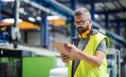 Technician or engineer with protective headphones standing in industrial factory, working. - HPIF15032