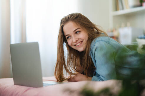 Schönes glückliches junges Mädchen mit Laptop auf dem Bett liegend und lächelnd, Online-Dating und Chatten Konzept. - HPIF15053