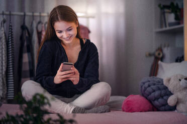 Frontansicht eines glücklichen jungen Mädchens, das ein Smartphone auf dem Bett benutzt, Online-Dating-Konzept. - HPIF15074