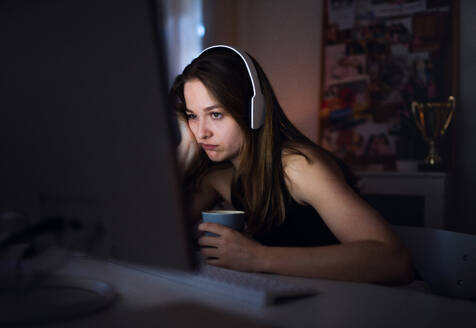Side view of bored young girl with headphones and computer sitting indoors, online chatting concept. - HPIF15089