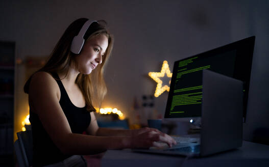 Side view of young girl with headphones and computer sitting indoors, online chatting concept. - HPIF15091