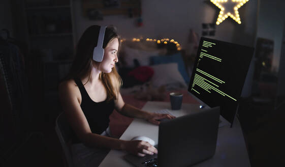 Young girl with headphones and computer sitting indoors, playing games and hacker concept. - HPIF15092