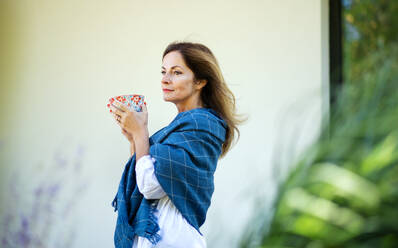 Seitenansicht einer reifen Frau mit einer Tasse Tee, die sich in einem Hinterhof ausruht. - HPIF15147