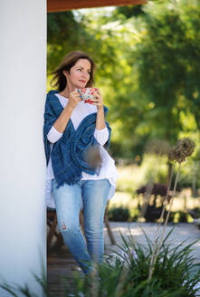 Side view of mature woman with cup of tea resting outdoors in backyard. - HPIF15148