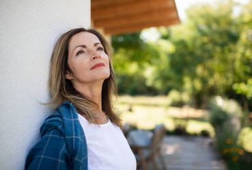 Portrait of mature woman resting outdoors, leaning on wall of house. - HPIF15149