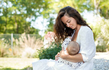 Portrait of woman nursing baby girl outdoors in backyard. - HPIF15159