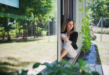 Vorderansicht einer reifen Frau, die im Büro in einem Containerhaus im Hinterhof arbeitet und sich ausruht. - HPIF15163