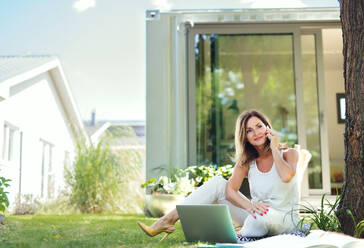 Mature woman working in home office outdoors in garden, using laptop and smartphone. - HPIF15171