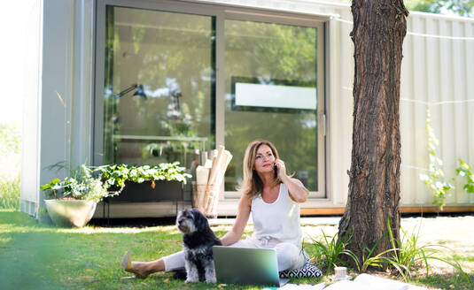 Reife Frau mit Hund, die im Home Office im Garten arbeitet und einen Laptop benutzt. - HPIF15172