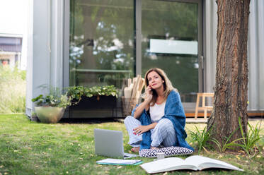 Mature woman in pajamas working in home office outdoors on grass in garden, using smartphone. - HPIF15177