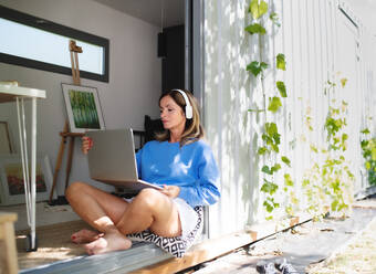 Front view of mature woman working in home office in container house in backyard. - HPIF15195